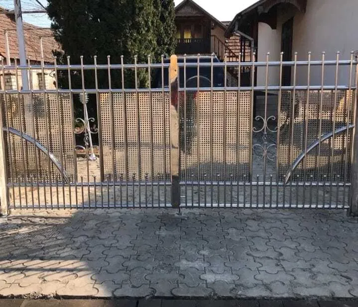 Металлические ворота с вертикальными прутьями, коваными завитками и перфорированными вставками у частного дома